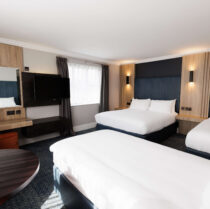 Bright hotel room with three inviting beds, a seating area, and a flat-screen TV.