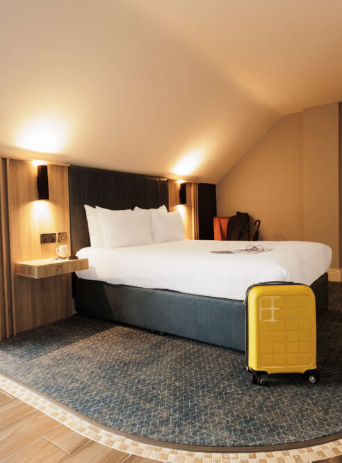 Cosy hotel room with a double bed and yellow suitcase.
