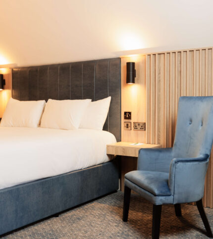 Elegant hotel room with plush bed and cosy armchair, illuminated by warm lighting.