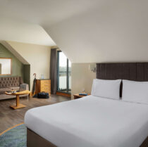 Inviting hotel room with a plush bed, seating area, and scenic window view.