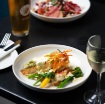 Gourmet meal with salmon, vegetables, beer, and wine at a cosy Springfield Hotel.