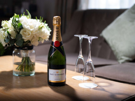 Elegant hotel suite with bubbly wine and flowers on a cosy table.