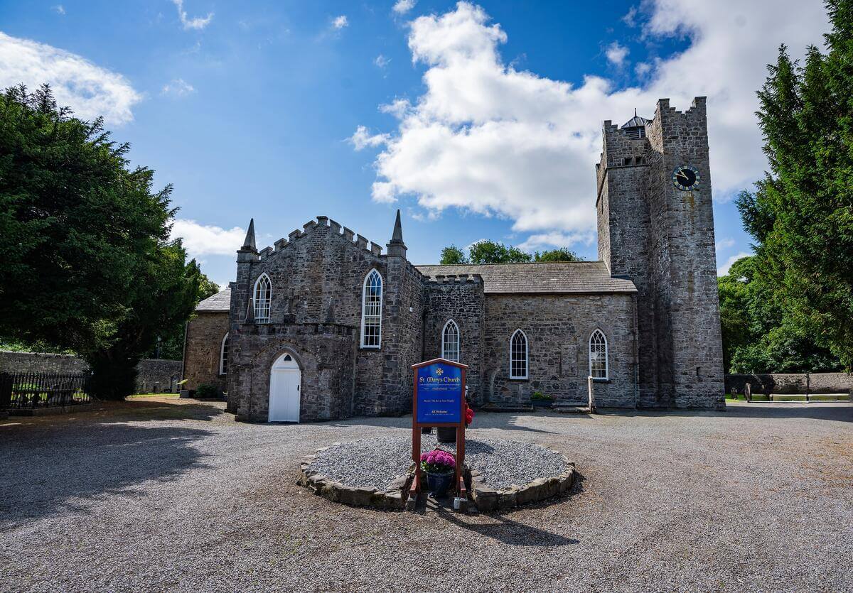 Historic stone church under a bright blue sky surrounded by lush greenery.