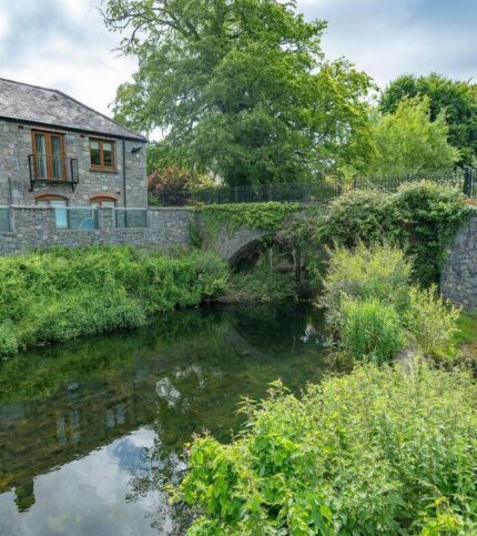 A family explores a charming stone hotel alongside a lush, green riverside garden.