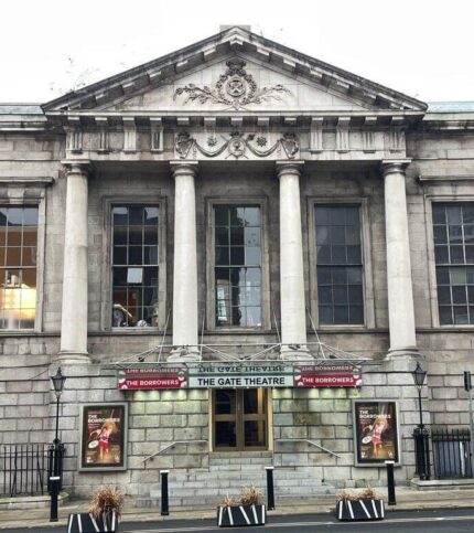 A historic stone building with columns, housing The Gate Theatre, Dublin. Street view with posters.