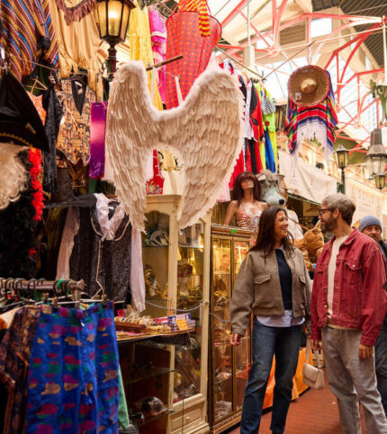 A couple explores a vibrant indoor market with colourful clothing and costumes.
