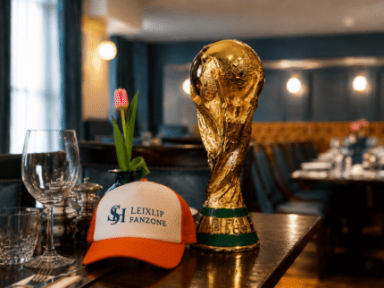 Cosy hotel dining setting with a colourful cap and trophy on a laid table.