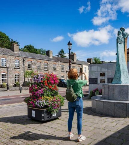 A woman photographs a statue in a charming, historic square with vibrant flowers.