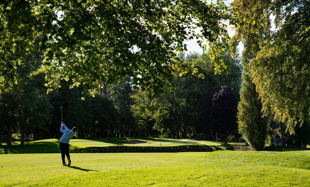 Person golfing on lush, green course surrounded by trees at Springfield Hotel.