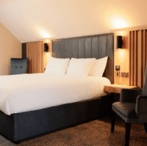 Elegant hotel room with a king-sized bed, warm lighting, and two cosy chairs.