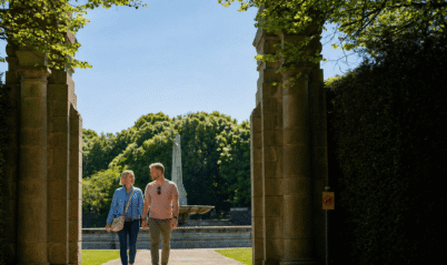 A couple walks hand in hand through a sunny garden at Springfield Hotel.