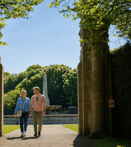 A couple walks hand in hand through a sunny garden at Springfield Hotel.