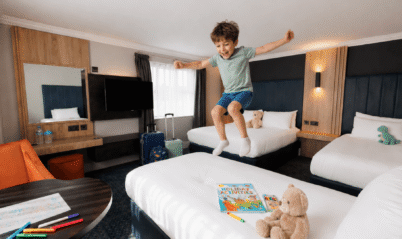 A joyful child jumps on a bed in a family-friendly hotel room with plush toys and activities.