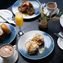 Elegant breakfast spread with eggs benedict, pancakes, coffee, and orange juice in a cosy setting.