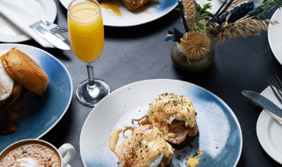 Um elegante café da manhã com ovos Benedict, panquecas, café e suco de laranja em um ambiente aconchegante.
