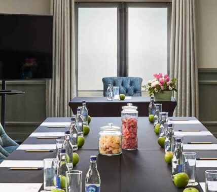 Elegant conference room setup with plush chairs, fruit jars, and notepads, ready for guests.
