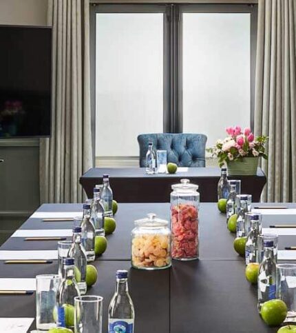 Elegant conference room setup with plush chairs, fruit jars, and notepads, ready for guests.