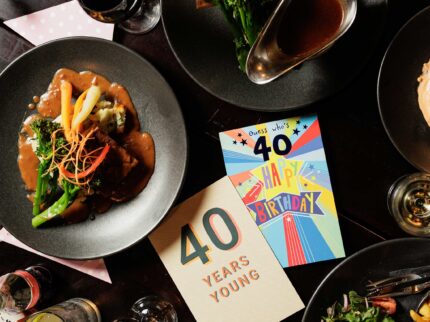 Family enjoying gourmet meal with colourful 'Happy Birthday' card on table.