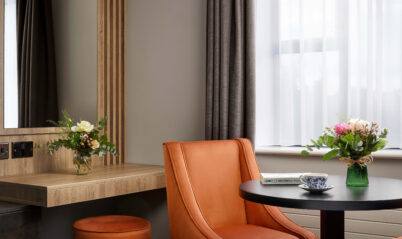 Cosy hotel room with a warm chair, flowers, and natural light from a window.