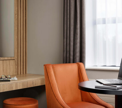 Cosy hotel room with a working desk, comfy chair, and laptop, perfect for relaxation or work.