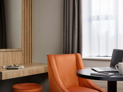 Cosy hotel room with a working desk, comfy chair, and laptop, perfect for relaxation or work.