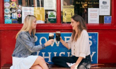Two friends enjoying drinks outside a cosy pub with vibrant red décor.