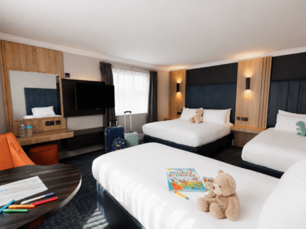 Spacious hotel room with double beds, children's toys, and travel guides on a sunny afternoon.