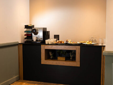 Cosy hotel breakfast nook with coffee machine and pastries.